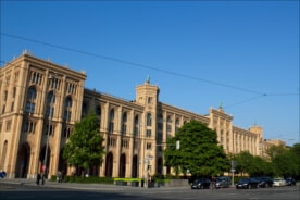 Gebäude der Regierungs Oberbayerns mit grünen Bäumen davor.