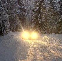 Ein Auto mit den eingeschalteten Scheinwerfer am Abend auf einer Waldstraße