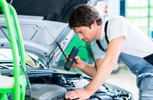 Fachmann bei der Prüfung unter der Motorhaube eines Autos beim Urlaubscheck